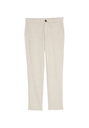 Gros plan sur la poche d’un pantalon beige à motif en chevrons porté avec un haut côtelé crème à manches longues.