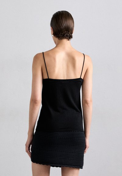 Black spaghetti strap top with a fitted design, made of a smooth fabric, paired with a textured, woven black mini skirt featuring a scalloped hem.
