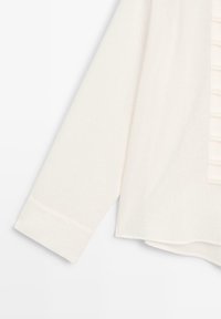 Weißer, strukturierter Pullover mit langen Ärmeln und rundem Saum. Die Vorderseite zeigt vertikale Knopfdetails und einen weichen, gemütlichen Stoff.