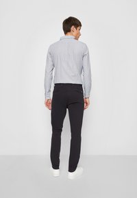 Blau-weiß gestreiften Button-up-Hemd, entspannte Passform, kombiniert mit schwarzen Hosen. Modell steht seitlich, trägt weiße Turnschuhe.