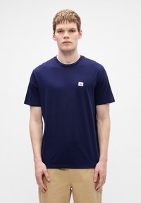 T-shirt azul-marinho de manga curta, feito de algodão, com um pequeno logótipo em branco e vermelho na zona do peito. Textura suave, design de gola redonda.