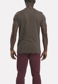 Camiseta de manga corta en color verde oliva, hecha de algodón suave, con un diseño sencillo. Se lleva con pantalones de chándal color marrón burdeos, que muestran un ajuste relajado y líneas limpias.