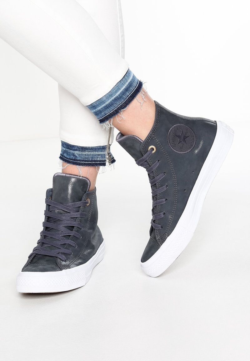 Baskets montantes en cuir gris foncé avec une finition texturée. Présentent une semelle en caoutchouc blanche et des lacets gris, rehaussés d'un logo circulaire.