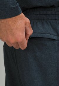 Tmavošedé športové nohavice s bočnou vreckom na zips; látka má štruktúrovaný vzhľad s elastickým pásom a jemnými švovými detailmi.