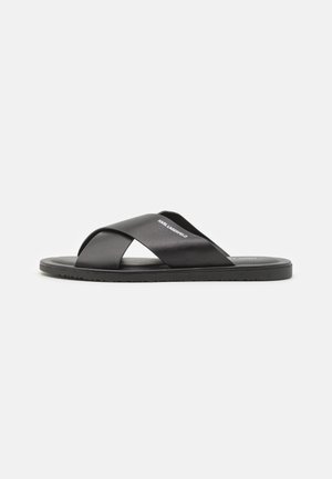Sorte sorte sandaler i svart med kryssede stropper laget av syntetisk materiale, med en glatt tekstur og en flat gummisåle.