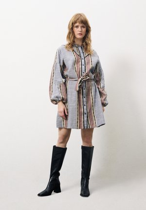 Grau gestreiftes Kleid mit tailliertem Gürtel, Knopfverschluss vorne und Puffärmeln. Schwarze knielange Stiefel runden den Look ab.