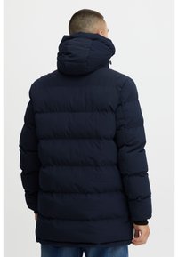 Tmavě modrá vatovaná bunda s kapucí, s prošívaným vzorem, silnou izolací a elastickými manžetami. Hladká tkanina s matným povrchem.