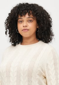 Light cream-colored knitted sweater featuring a cable-knit design with open weave detailing and a crew neck.