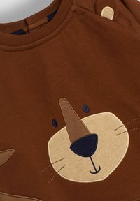 Brązowa bawełniana bluza z nadrukiem w kształcie twarzy lwa, z beżowym nosem, ciemnoniebieskim nosem i haftowanymi wąsami; okrągły dekolt z zatrzaskami.
