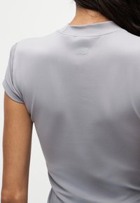 Vue de dos d’une personne portant un t-shirt gris clair à manches courtes avec un petit logo New Balance sous l’encolure.