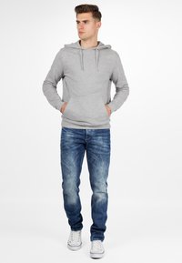 Sweat à capuche gris avec cordon de serrage, poche avant, et poignets côtelés ; associé à un jean en denim bleu délavé et des baskets blanches.