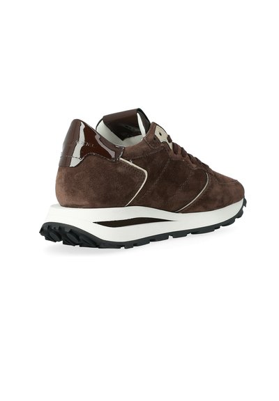 Sneaker in suede marrone con suola bianca, battistrada nera e dettaglio lucido in marrone scuro sul tallone, orientato a destra su sfondo bianco.