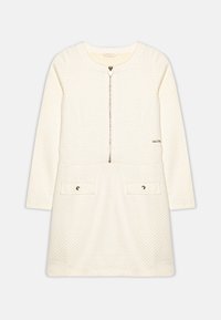 Elfenbeinfarbenes Kleid mit langen Ärmeln, strukturierter Stoff, goldenes Punktmuster, Frontreißverschluss und zwei Akzenttaschen mit goldenen Hardware-Details.