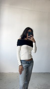 Top de malha branca sem alças com tecido preto drapeado, mangas longas com detalhes em botão, combinado com jeans azul claro.