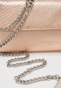 Metallic roséguld axelväska med en strukturerad ormskinnsprint, med en silverkedjesnor och präglad logotyp.