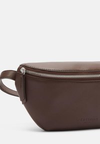 Borsetta in pelle marrone con texture liscia, chiusura con zip e manico laterale. Presenta un marchio in rilievo sul davanti. Design compatto e slanciato.