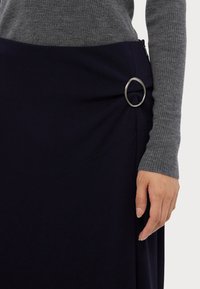 Navy skirt made of smooth fabric with diagonal stitching and a silver metal ring accent, paired with a gray ribbed long-sleeve top.