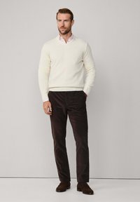 Hellbeige V-Ausschnitt-Pullover, hellrosa Hemd mit Kragen, braune Kordhose, braune Wildleder-Loafers. Glatte Textur und klassisches Design.