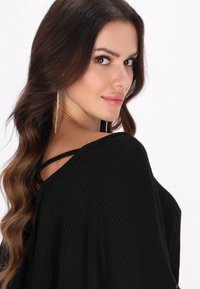 Top nero lavorato a maglia con una vestibilità rilassata, caratterizzato da un ampio scollo e dettagli incrociati sulle spalle. Tessuto morbido e leggero.