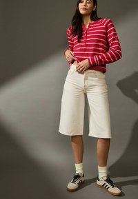 Camicia a maniche lunghe a righe rosse e bianche abbinata a jeans cropped a gamba larga color crema e sneakers nere con suola color tan.