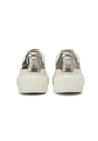 Białe trampki na platformie z grubymi żebrowanymi podeszwami, z metalicznymi srebrnymi panelami pięty z wytłoczonymi logo, widziane od tyłu.