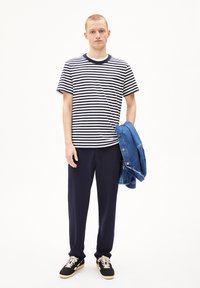 T-shirt a righe navy e bianche, pantaloni navy, sneakers nere con lacci crema e giacca di denim blu. Tessuto morbido, vestibilità casual.
