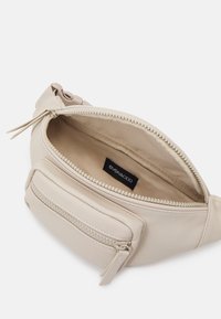 Béžová kabelka z umělé kůže s hlavním oddílem na zip a přední kapsou, s hladkou texturou a nenápadnou značkovou cedulkou uvnitř.