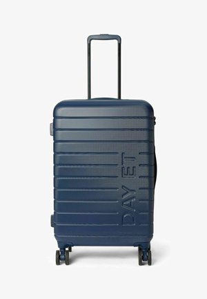 Valise rigide bleu marine à surface texturée, avec des rainures horizontales, le nom de la marque embossé, une poignée rétractable et quatre roues pour une mobilité aisée.