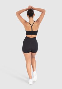 Sujetador deportivo negro con tirantes finos y pantalones cortos deportivos negros de tiro alto. Tela suave y un diseño ajustado, combinados con zapatillas deportivas blancas.