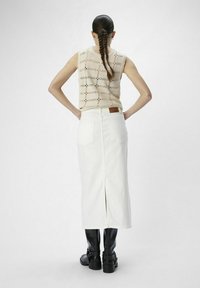 Vit denim midi kjol med en slits bak, kombinerad med en ljus stickad topp med perforerat mönster, och svarta knähöga stövlar.