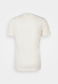 Gładka, biała bluzka z krótkim rękawem widoczna z tyłu na jasnym tle, bez widocznych logo ani wzorów.