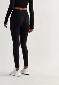 Black high-waisted leggings with textured surface, fitted design, and stretchy material, paired with white athletic shoes.
