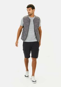 Grå quiltet vest med et tekstureret mønster, grå stribet t-shirt, sorte cargo shorts og hvide sneakers med marineblå detaljer.
