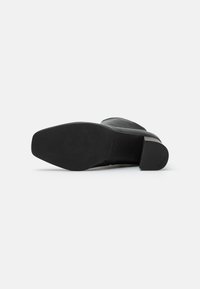 Botín negro de tacón con un acabado mate suave, punta redonda y suela de goma texturizada. Diseño minimalista sin adornos visibles.
