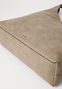Beige mockaskhandväska med mjuk textur, rektangulär form och ett guldlogo. Har en enkel, ren design med minimal sömnad.