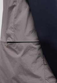 Leichte Jacke aus einem grauen, strukturierten Stoff mit glatten, navyfarbenen Ärmeln und einer dezenten, mit Reißverschluss versehenen Tasche zur Aufbewahrung.