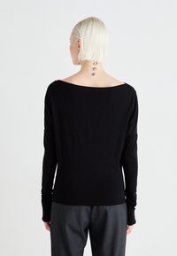 Black long-sleeve top featuring a wide neckline and loose fit. Made of soft fabric with a smooth texture. Pairing with gray pants.