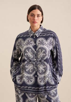 Marineblå skjorte med hvide paisley-mønstre, lange ærmer og knaplukning. Stoffet ser blødt ud med en glat overflade.