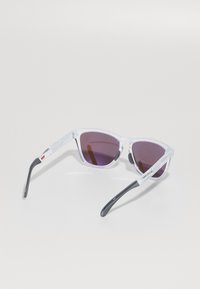 Occhiali da sole chiari e angolari con lenti viola scuro e aste nere. Montatura in plastica leggera. Design minimalista con un sottile dettaglio del logo.