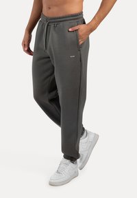 Grå sweatpants med elastisk talje og sidelommer, med ribbede ankler. Sammen med hvide sneakers.
