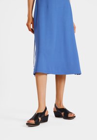 Sandali con zeppa neri, con punta aperta e ritagli laterali, dotati di una tomaia in pelle liscia e una suola chiara. Abbinati a un vestito blu.