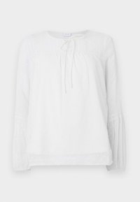 Camicia bianca con lunghe maniche a sbuffo, tessuto testurizzato con pois, scollatura rotonda e lacci sul davanti. Dettagli in pizzo alle spalle.