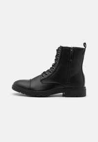 Botas de ante negras con punta redonda, cordones en la parte delantera, cremallera lateral y suela texturizada, con ojales plateados y una pestaña para tirar.