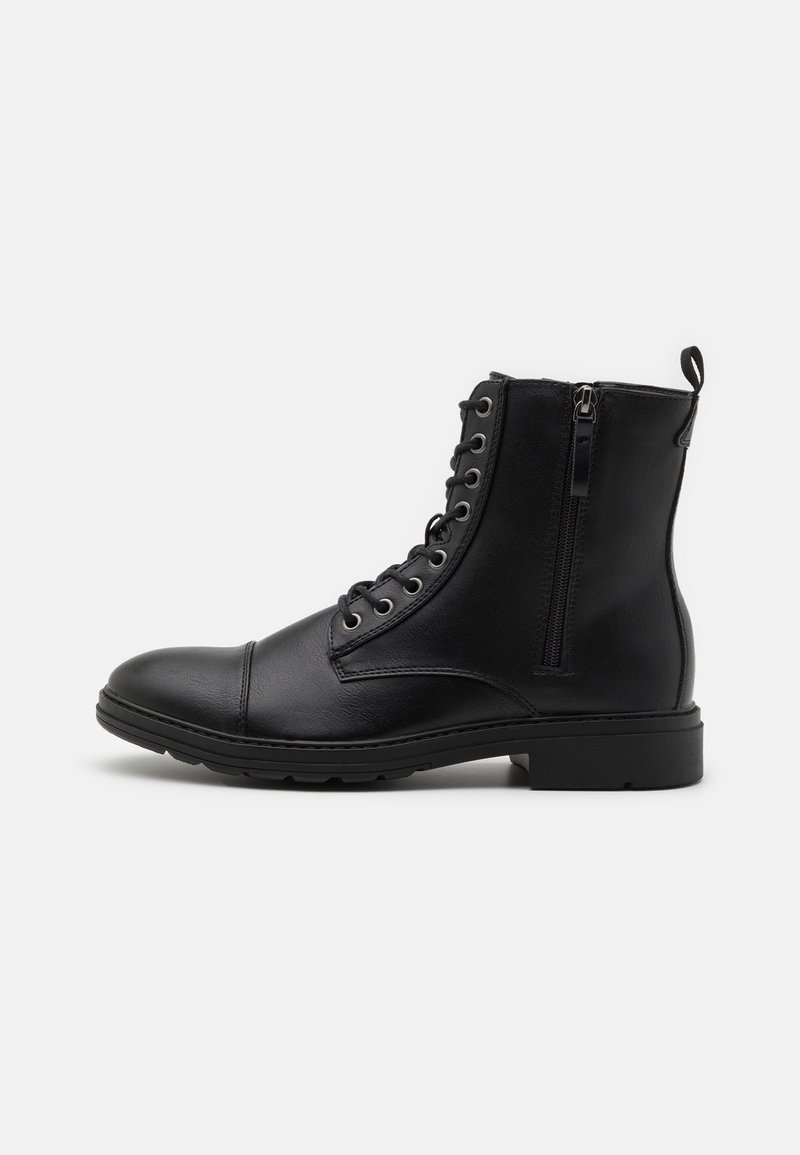 Botas de ante negras con punta redonda, cordones en la parte delantera, cremallera lateral y suela texturizada, con ojales plateados y una pestaña para tirar.