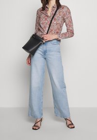 Camisa de botones con estampado floral, jeans de pierna ancha en azul claro, bolso de cuero negro tipo bucket con correa y tacones negros con tiras.