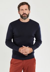 Marineblauwe gebreide trui met een ronde halslijn, voorzien van vier knopen op één schouder en aansluitende lange mouwen.