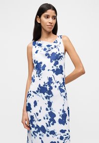 Φόρεμα χωρίς μανίκια σε λευκό με μπλε αφηρημένο λουλουδένιο σχέδιο, με λαιμόκοψη καπέλο και απαλό ύφασμα, εφαρμοστό στο σώμα.