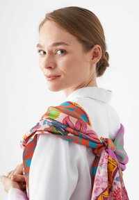 Zijde sjaal over een wit shirt gedrapeerd, met levendige bloempatronen in roze, oranje en teal, met een zachte textuur en vloeiend ontwerp.