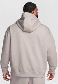 Sweatshirt à capuche gris clair avec une coupe décontractée, des poignets côtelés et une poche kangourou à l'avant. Tissu lisse et détails de couture minimalistes.