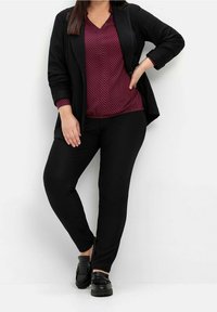 Svart blazer över en vinröd mönstrad topp, parat med svarta åtsittande byxor och svarta slip-on skor. Slät textur och skräddarsydd passform genomgående.